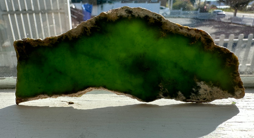 Irregular green mineral slab with a rough beige edge on a windowsill.