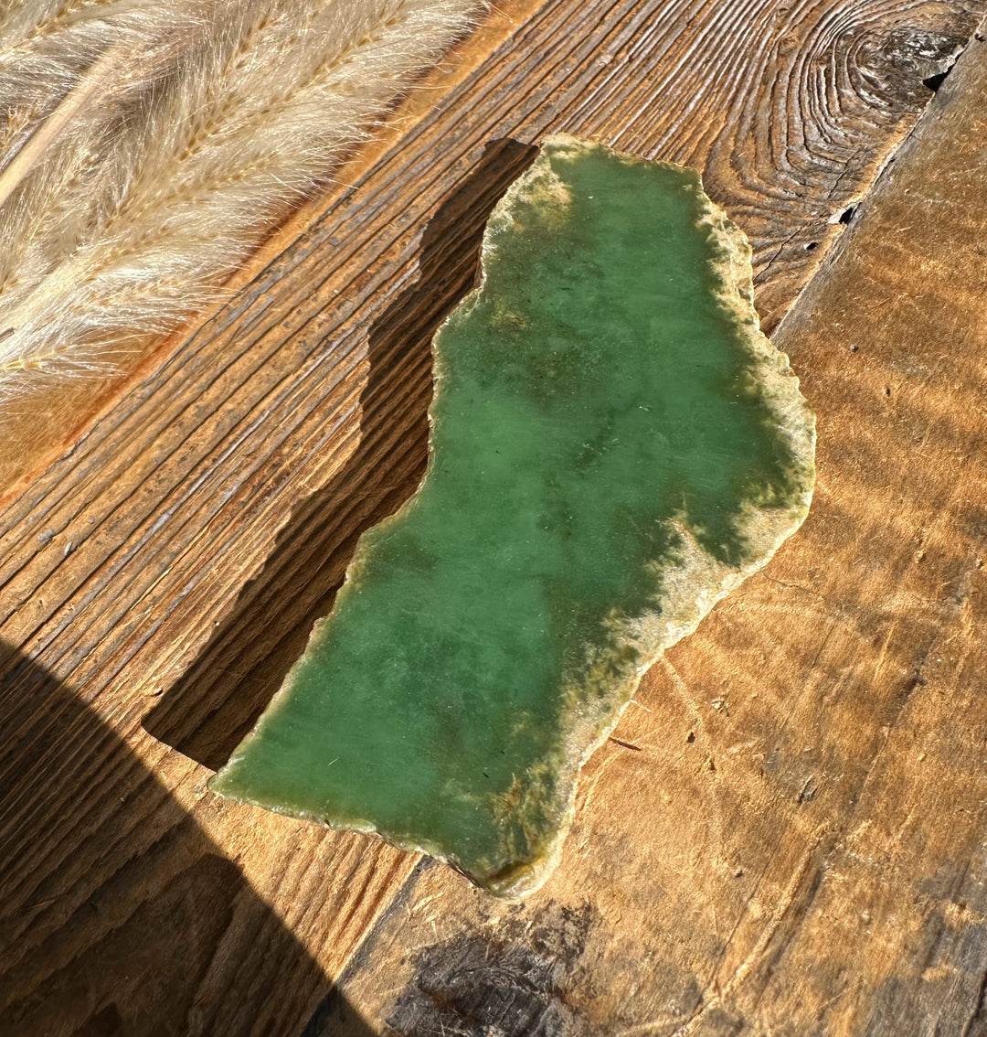 Green jade-like stone slab with rough edges on a weathered wooden surface.