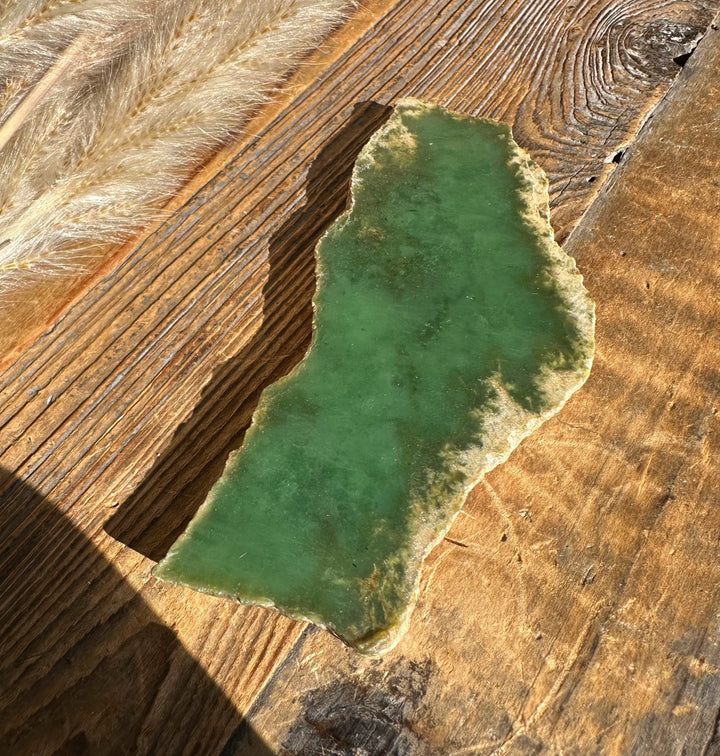 Green jade-like stone slab with rough edges on a weathered wooden surface.