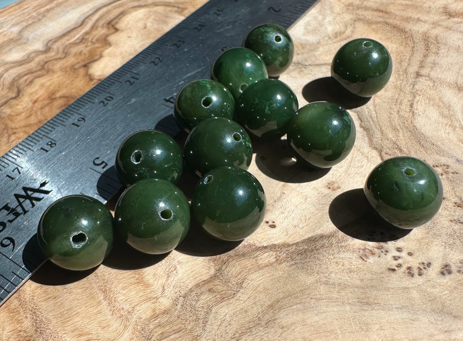 Cluster of 14mm Canadian Cassiar jade beads with drilled holes on a wooden surface beside a ruler
