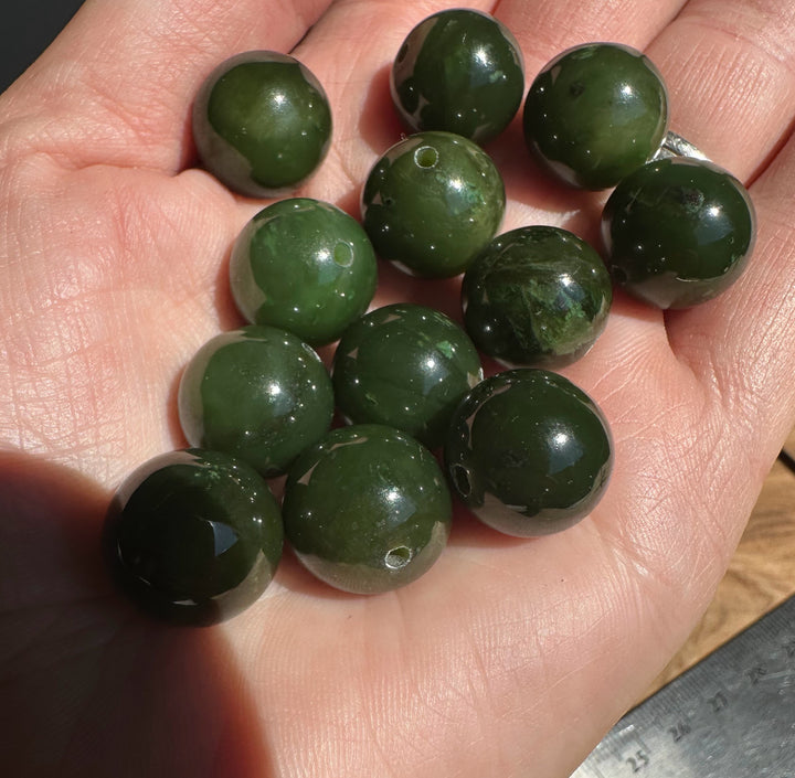 Several 14mm Canadian Cassiar jade beads held in a hand with visible drilled holes for threading