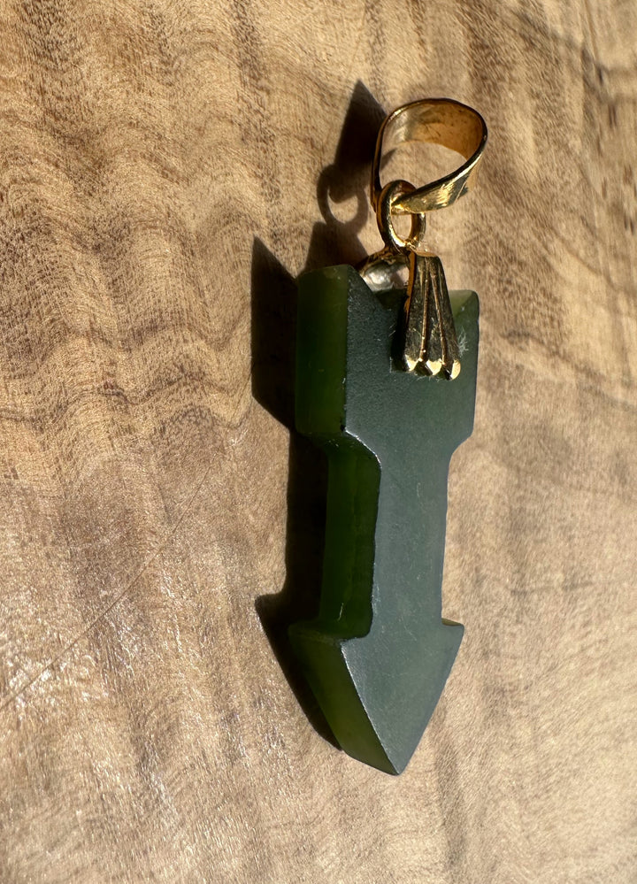 Green arrow-shaped pendant with a gold chain on a wooden surface