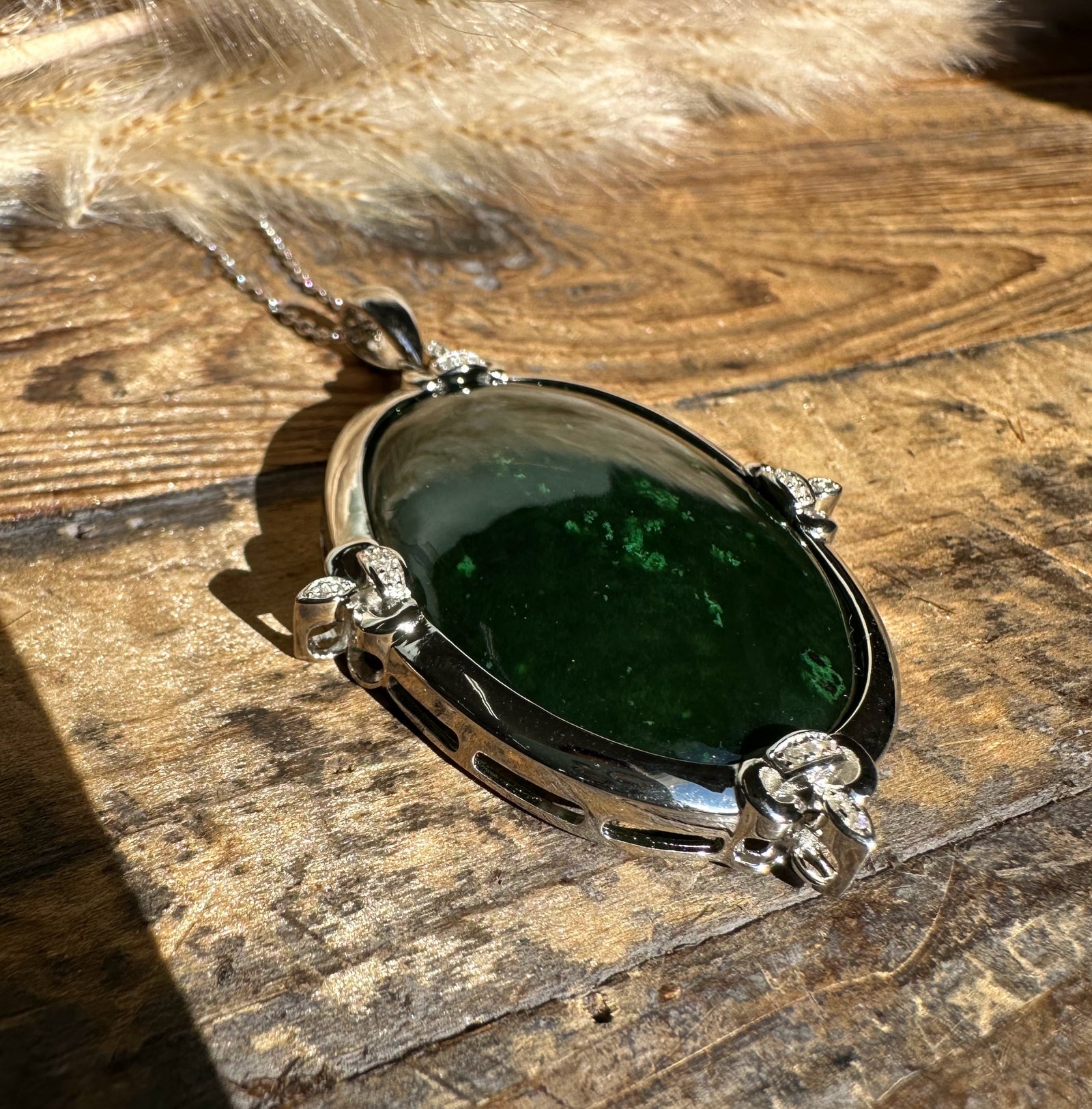 Canadian Jade and Zircon Pendant with dark green oval jade set in a silver bezel with zircon accents on a wood surface