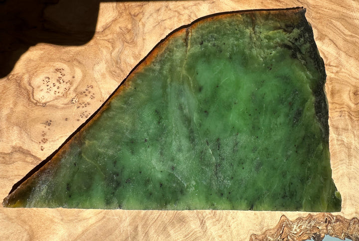 Siberian nephrite jade slab in green with brown rim on wood surface