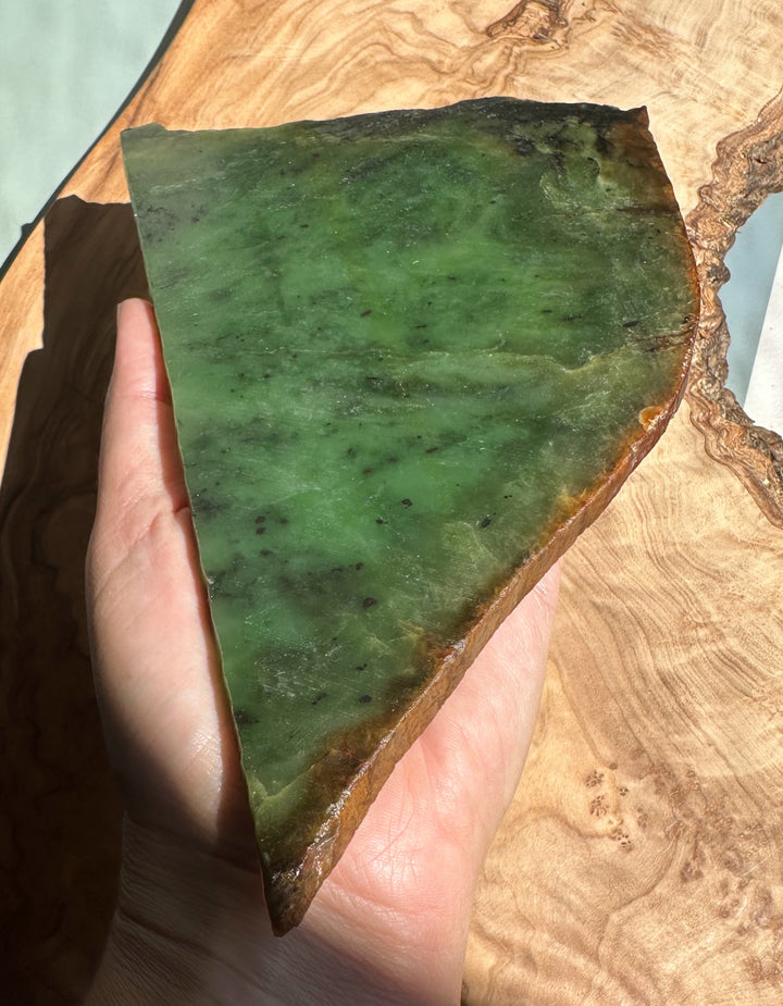 Siberian nephrite jade slab held in hand, green with a brown edge against a wooden background.