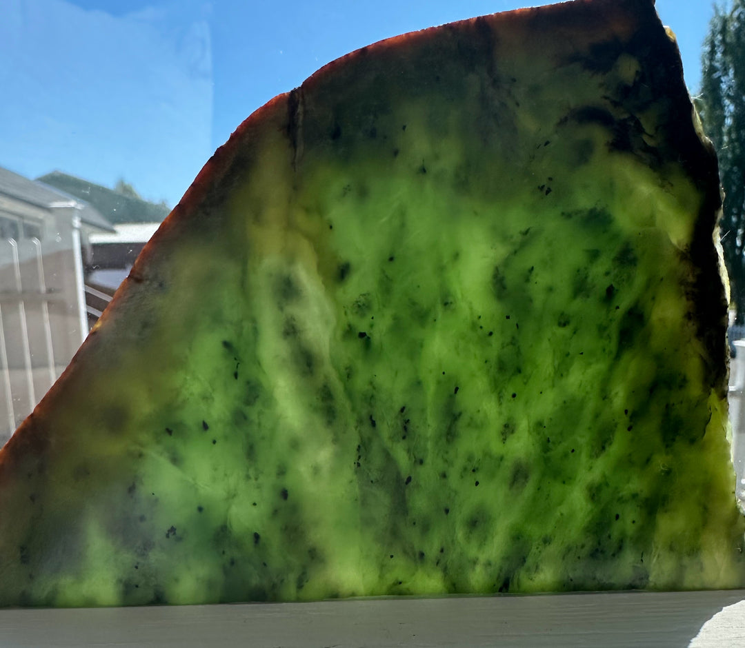 Siberian nephrite jade slab with bright green translucence and dark speckles and brown edge