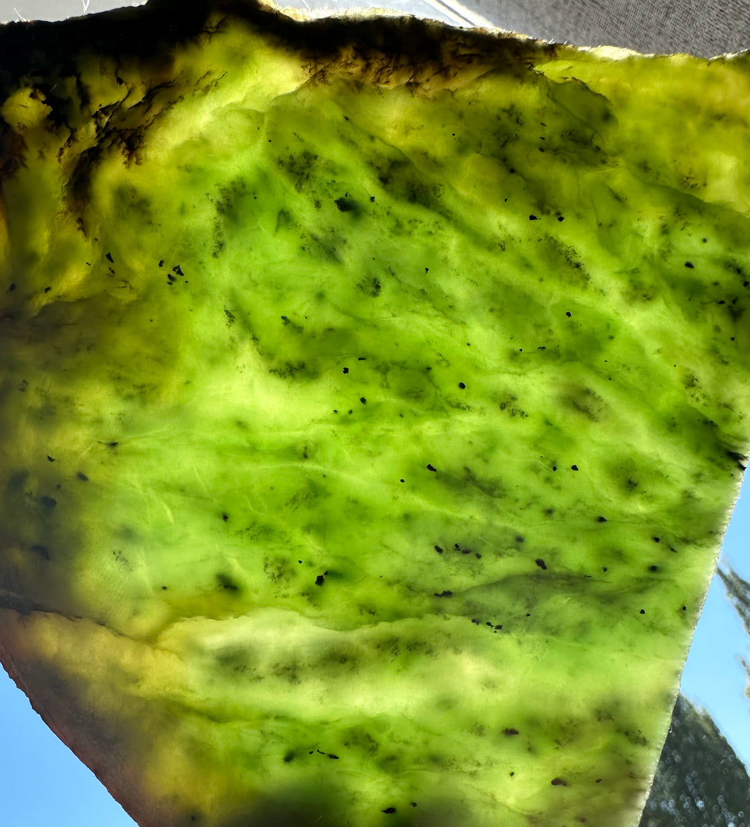 Close up of neon green Siberian nephrite jade showing translucent texture and dark specks.