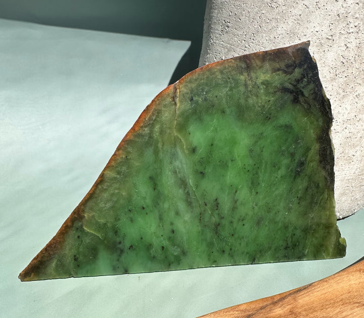 Triangular slab of Siberian nephrite jade with vibrant green color and brown rim against a pale surface.