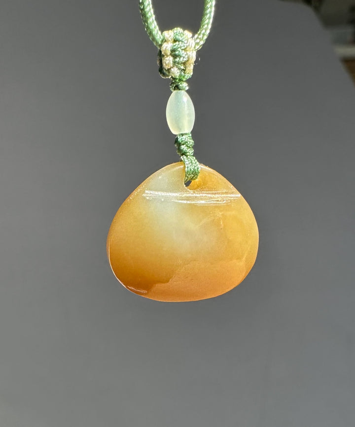 Pale jade bead above an orange teardrop pendant on a knotted green braided cord