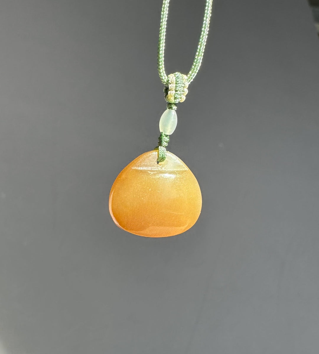 Green braided necklace with a knot and a small jade bead above a larger pendant against a gray backdrop.