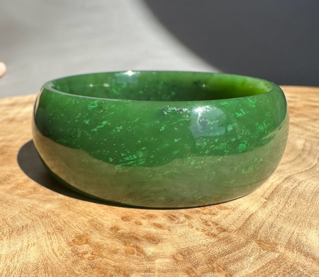 Green cassiar jade bangle resting on a wooden surface