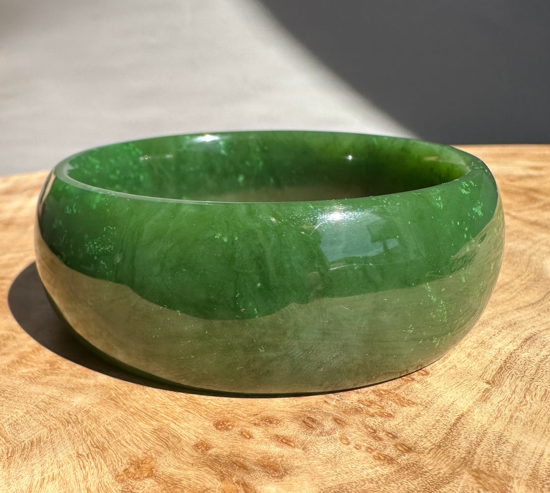 A Grade Cassiar Jade Bangle in rich green rests on a wooden surface