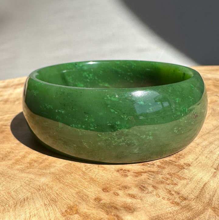 Close up of a green jade bangle with surface markings on a wooden surface.