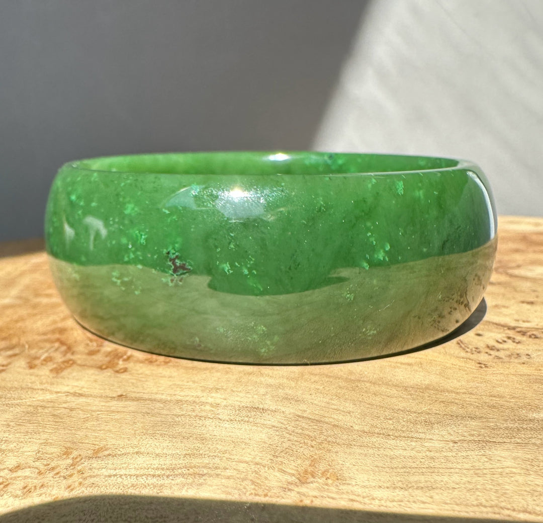 Side view of a green jade bangle against a neutral gray backdrop.