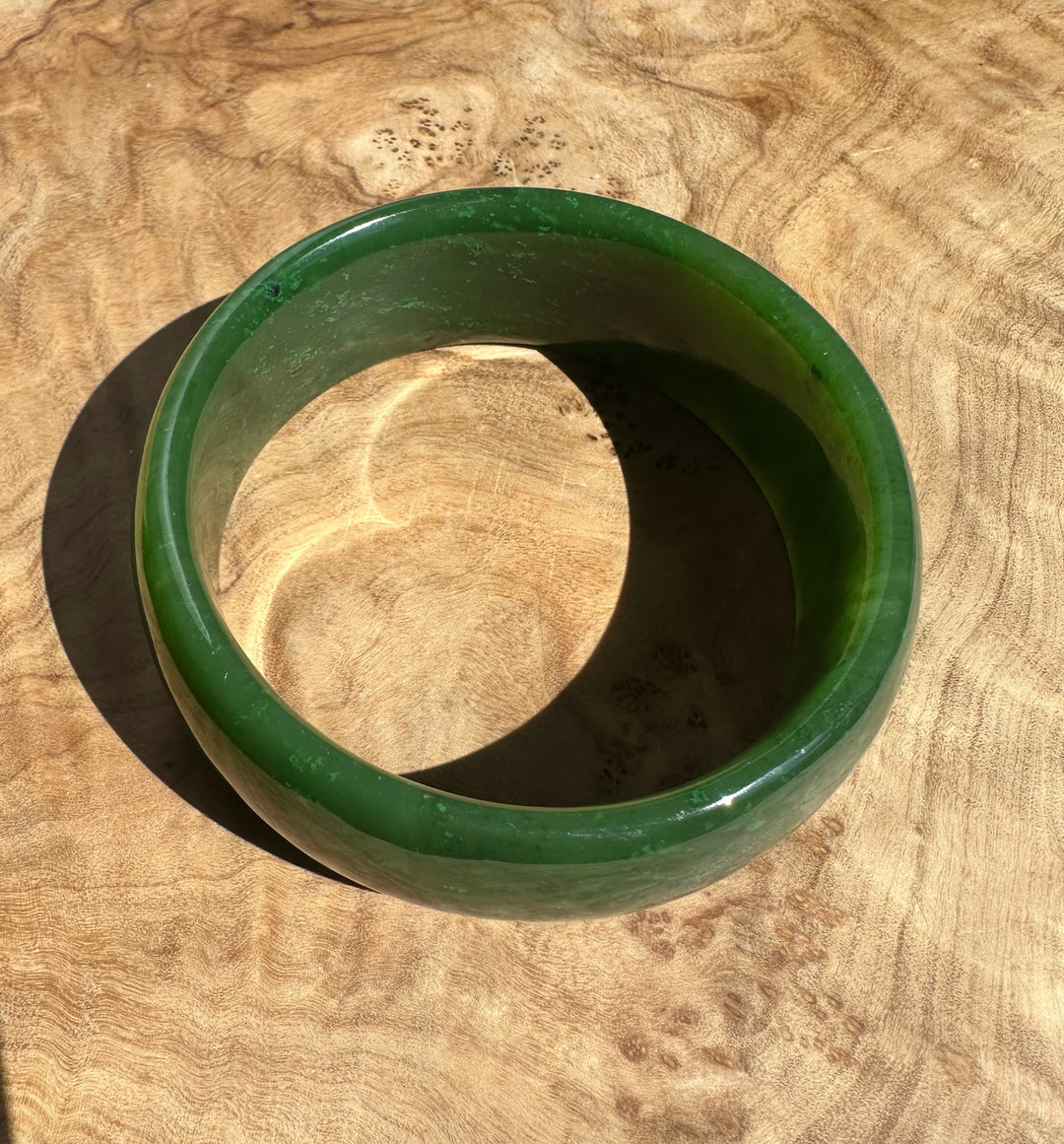 Glossy green Cassiar jade bangle resting on a textured wood surface.