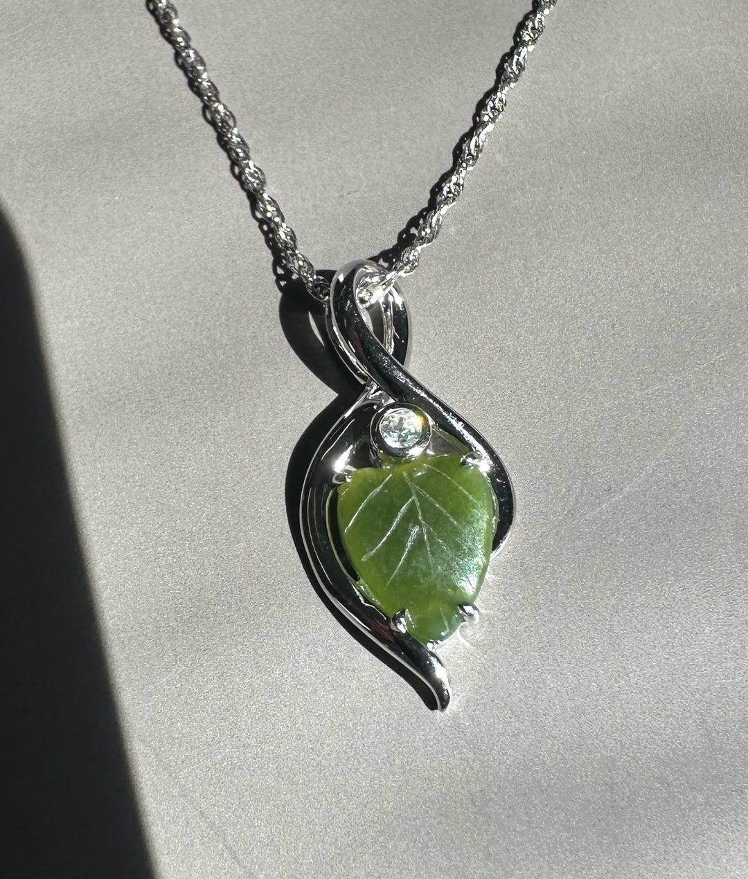 Silver infinity pendant with a green jade leaf on a silver chain.