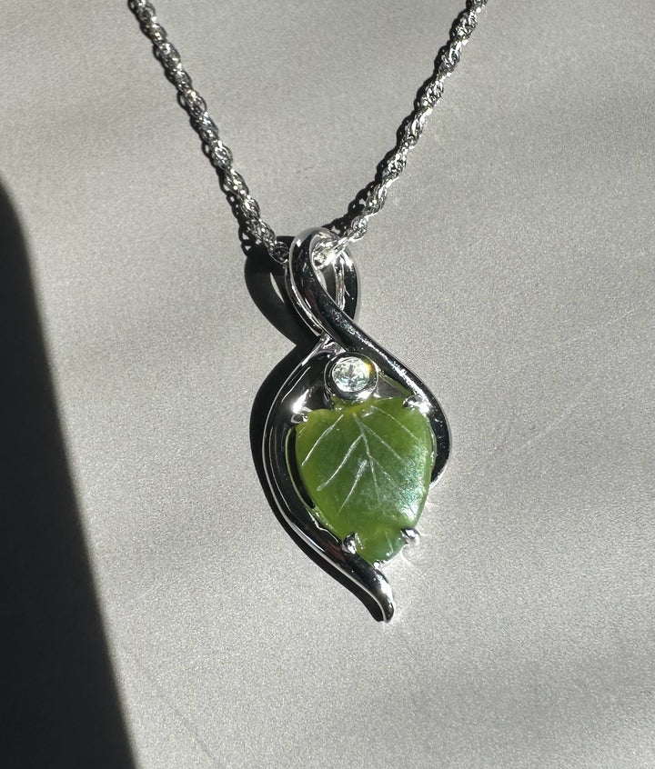 Silver infinity pendant with a green jade leaf on a silver chain.
