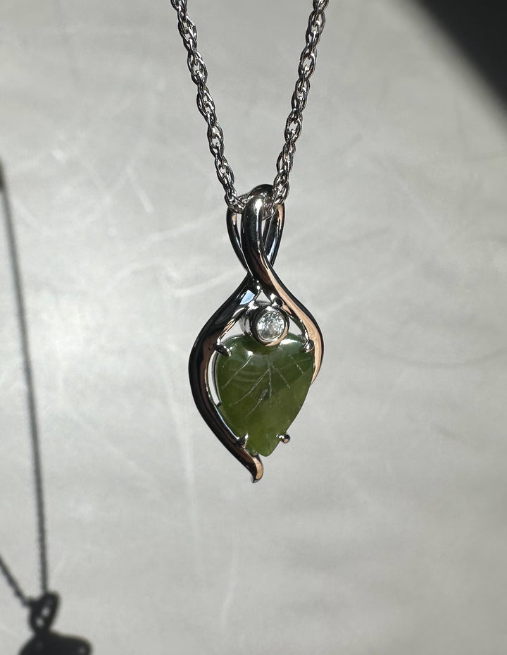 Close up of the pendant on a chain showing the green jade leaf and silver infinity curves against a pale background