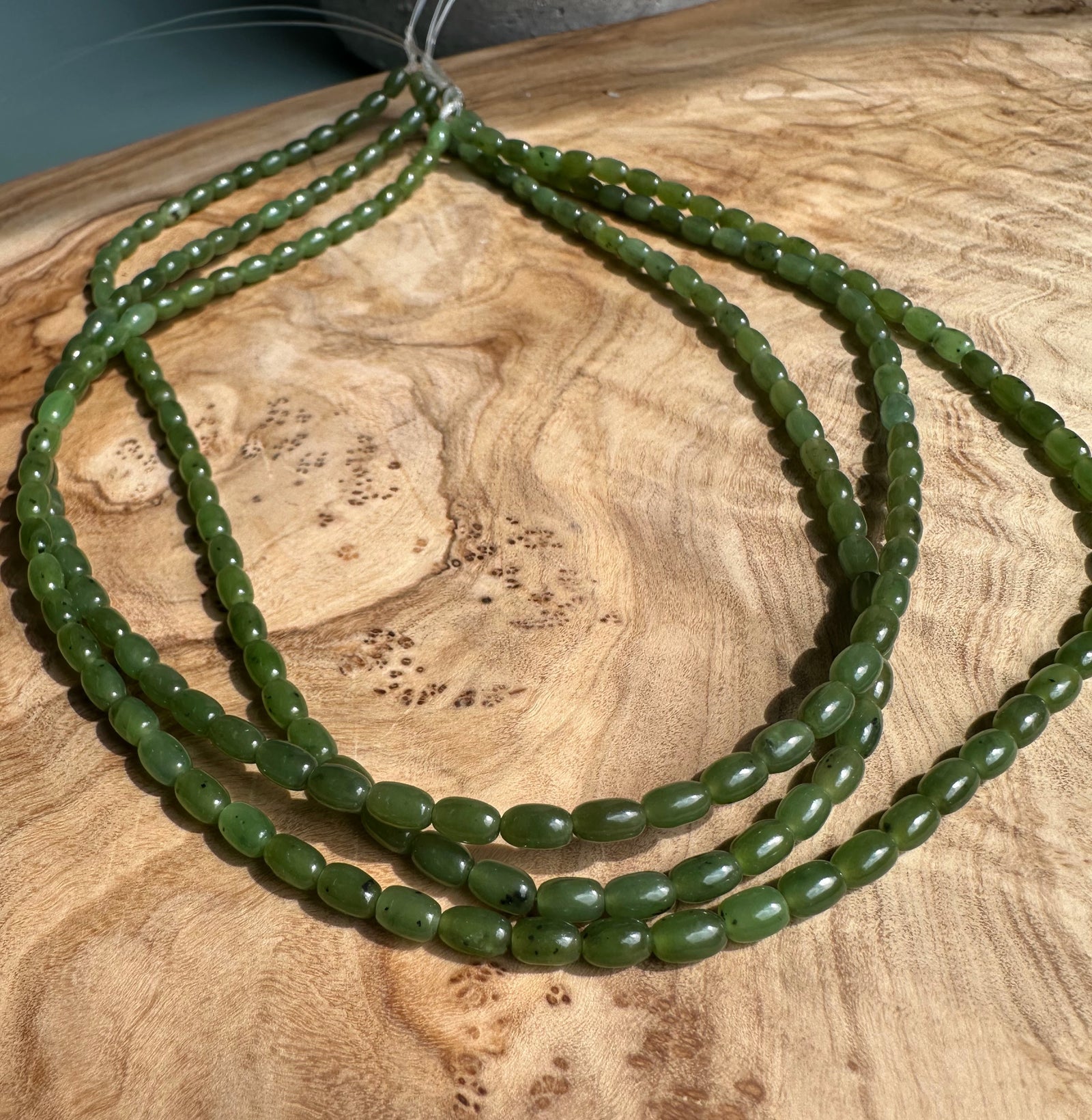 Several strands of glossy green jade beads 6x4mm laid across a wooden surface