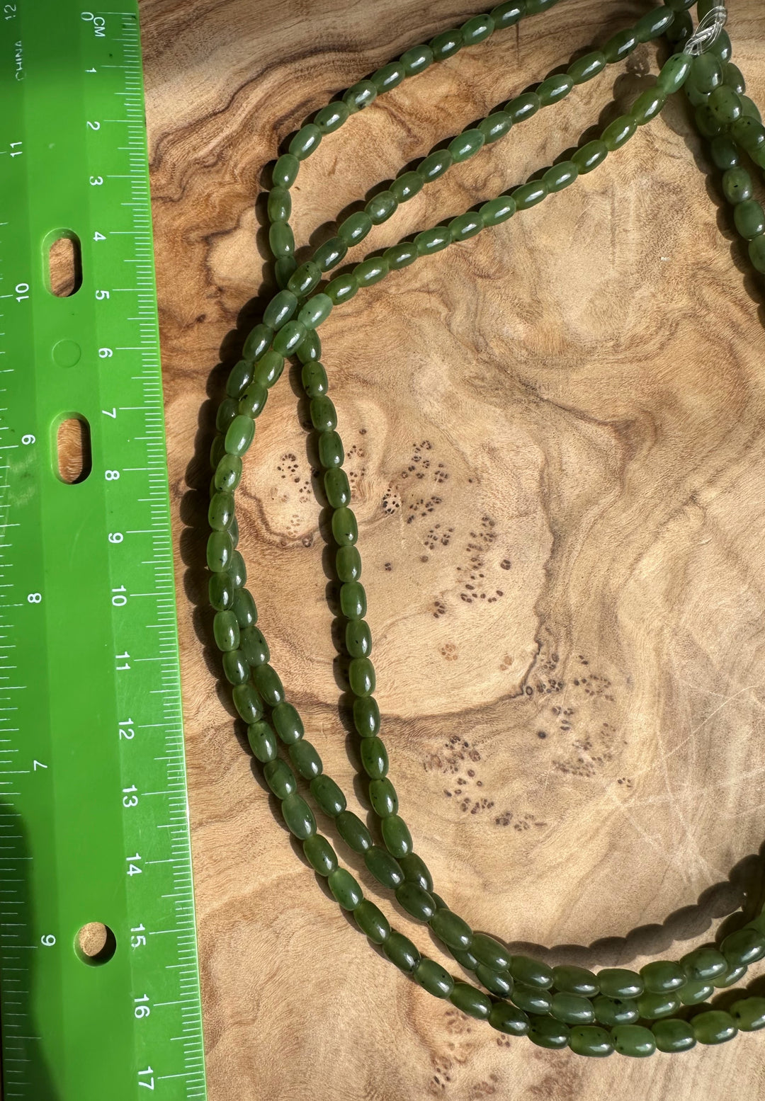 Canadian Jade beads 6x4 mm beside a green ruler on a wood background