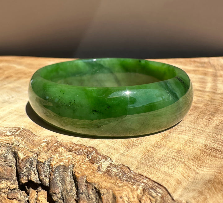 Jade Bangle 56 x 17mm in vibrant green resting on a wooden surface against a warm brown background