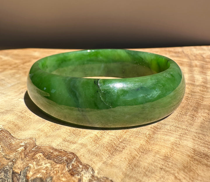 Jade bangle 56 x 17mm in vivid green resting on a wooden surface