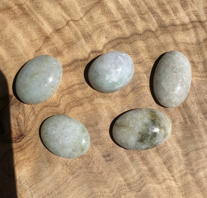 Group of pale blue green jadeite cabochons arranged on a textured brown surface