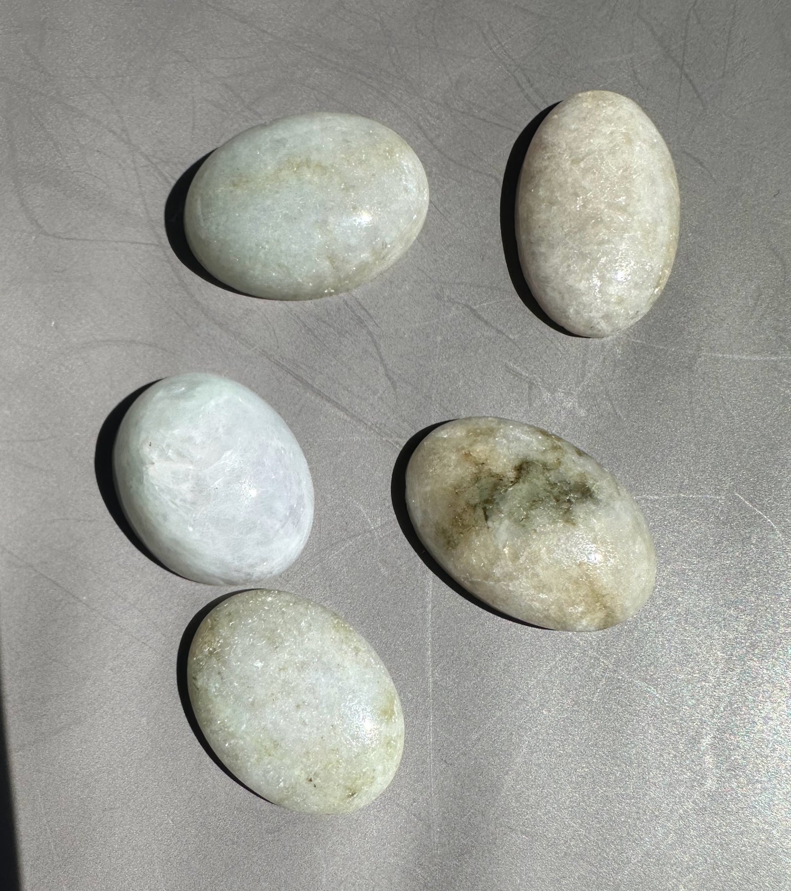 Five pale green Burmese jadeite cabochons arranged on a gray surface for scale