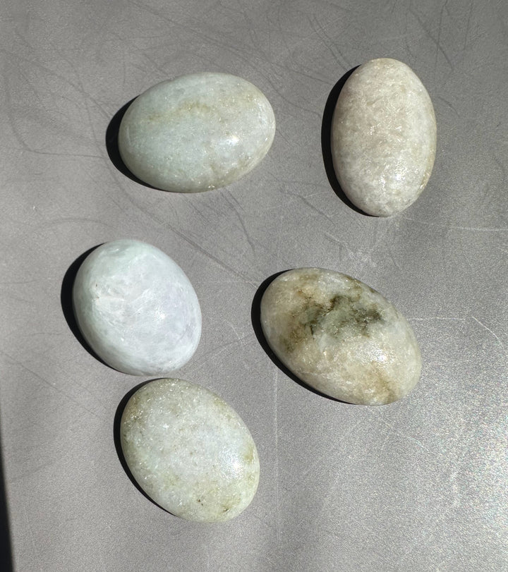 Five pale green Burmese jadeite cabochons arranged on a gray surface for scale
