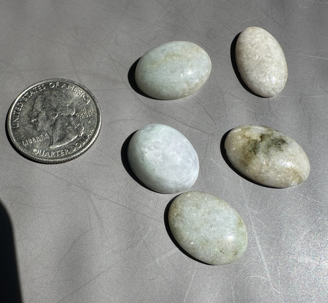 Two smooth jadeite cabochons on a gray surface with a partial quarter nearby