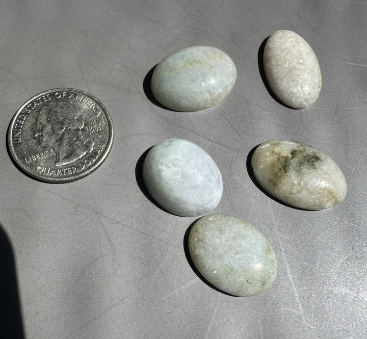 Two smooth jadeite cabochons on a gray surface with a partial quarter nearby