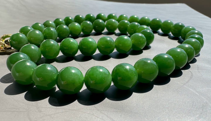 Green polished 10mm beads arranged in a loose coil on a gray surface unstrung