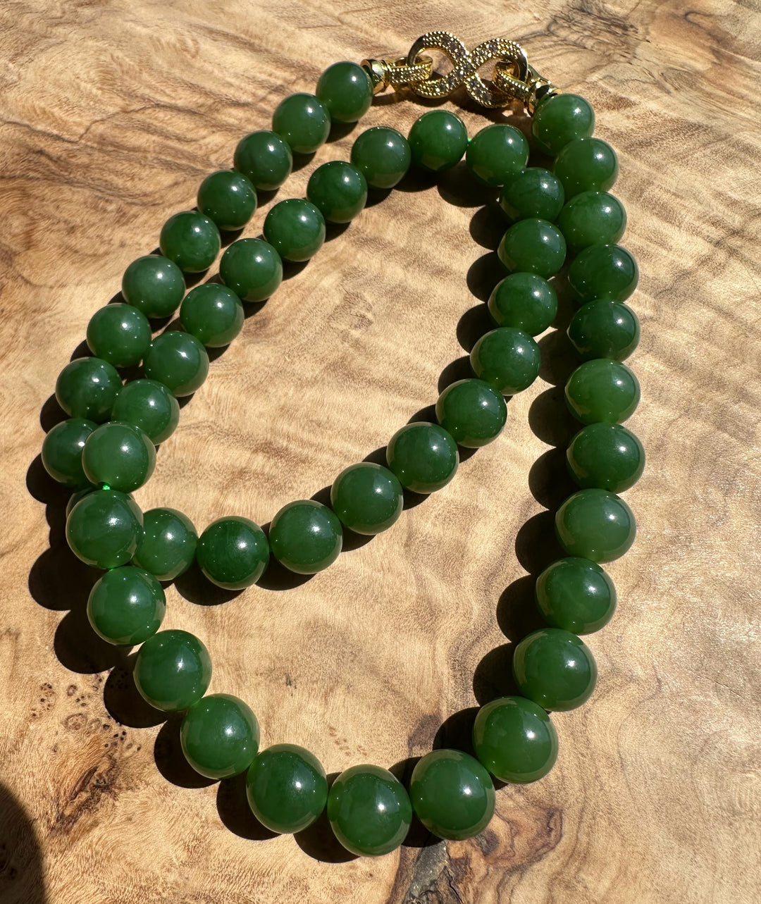 Green 10mm beads with a gold clasp forming a loop on a wood background