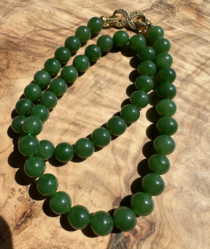 Green 10mm beads with a gold clasp forming a loop on a wood background