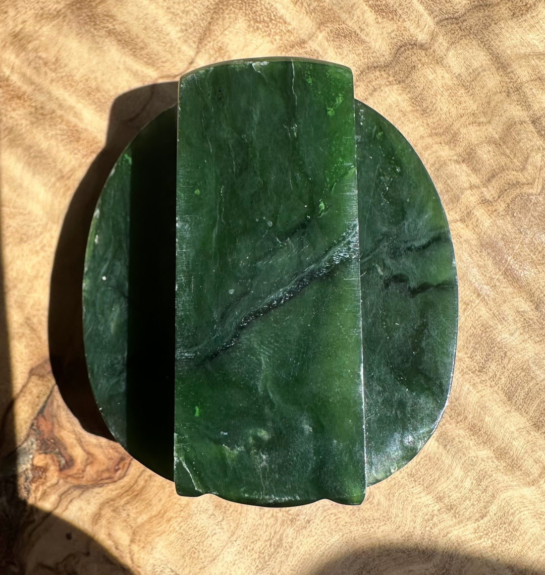 Close up of a dark green jade belt buckle with a curved top edge resting on a brown surface
