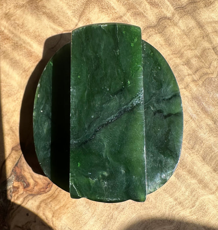 Close up of a dark green jade belt buckle with a curved top edge resting on a brown surface