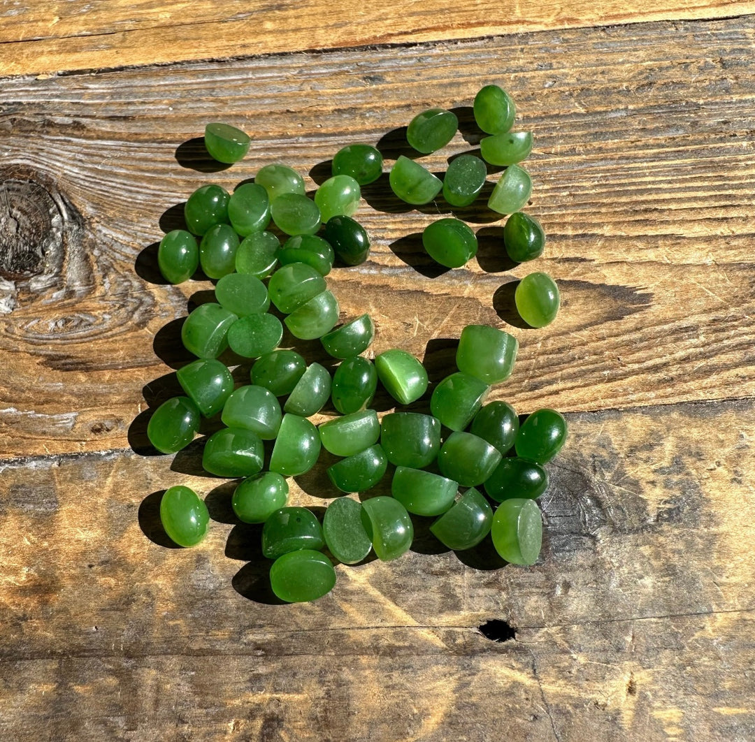 Green jade cabochons 8x6mm high dome spread on a rustic wooden surface