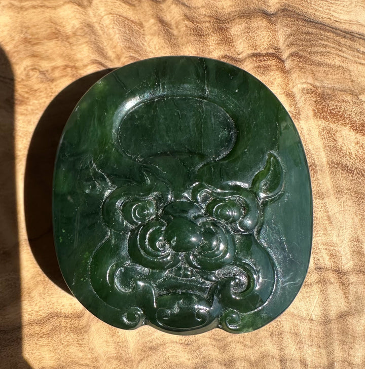 Circular jade belt buckle in deep green with carved detailing on a wooden surface