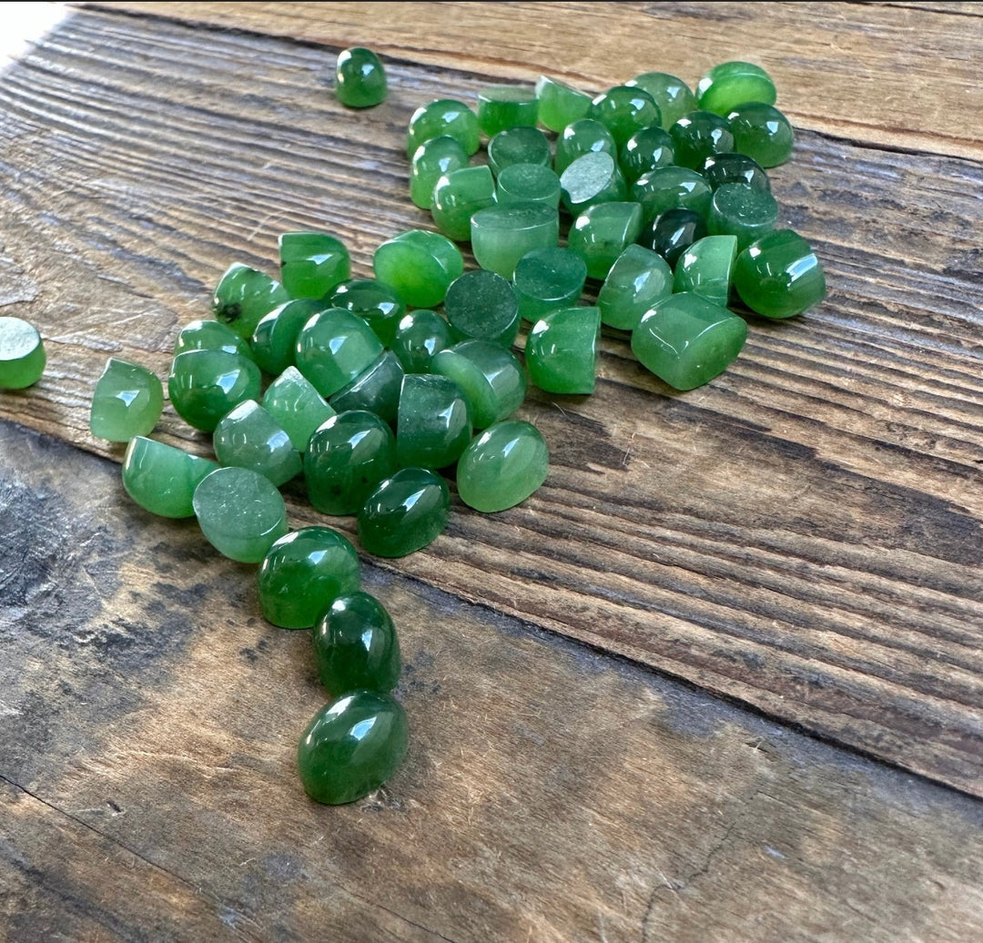 Cluster of small green jade cabochons scattered on a rustic wooden surface