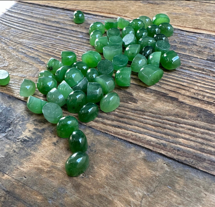 Cluster of small green jade cabochons scattered on a rustic wooden surface