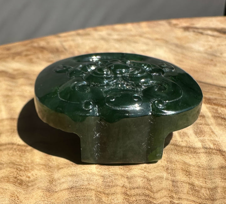 Jade belt buckle in dark green with carved motifs placed on a textured wooden surface