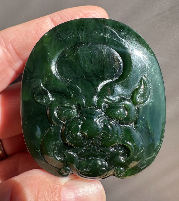 Intricate dragon carved in deep green jade belt buckle held by fingers