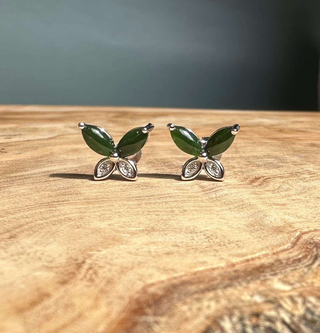 Pair of silver butterfly stud earrings with emerald green stones and crystal wings displayed on wood