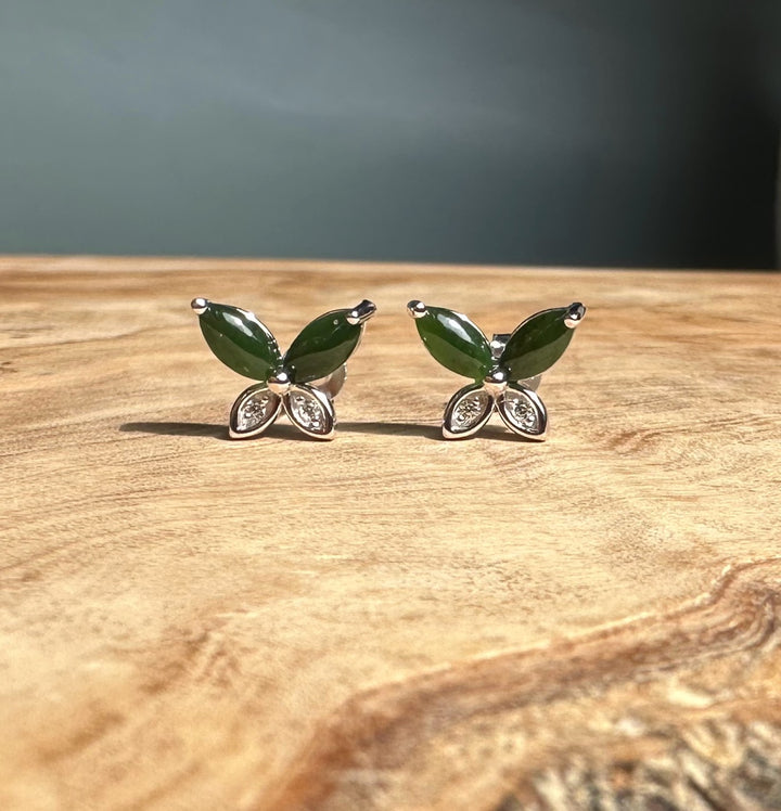 Pair of silver butterfly stud earrings with emerald green stones and crystal wings displayed on wood