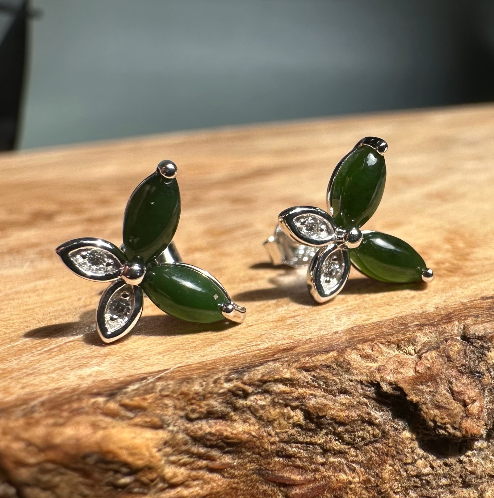 Silver butterfly stud earrings with dark green marquise stones and crystal accents on a wooden surface