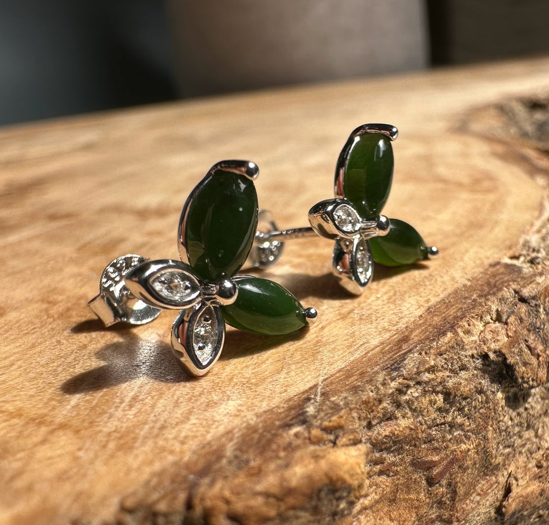 Close-up of silver butterfly stud earrings showing green stones and crystal accents on a wooden slab