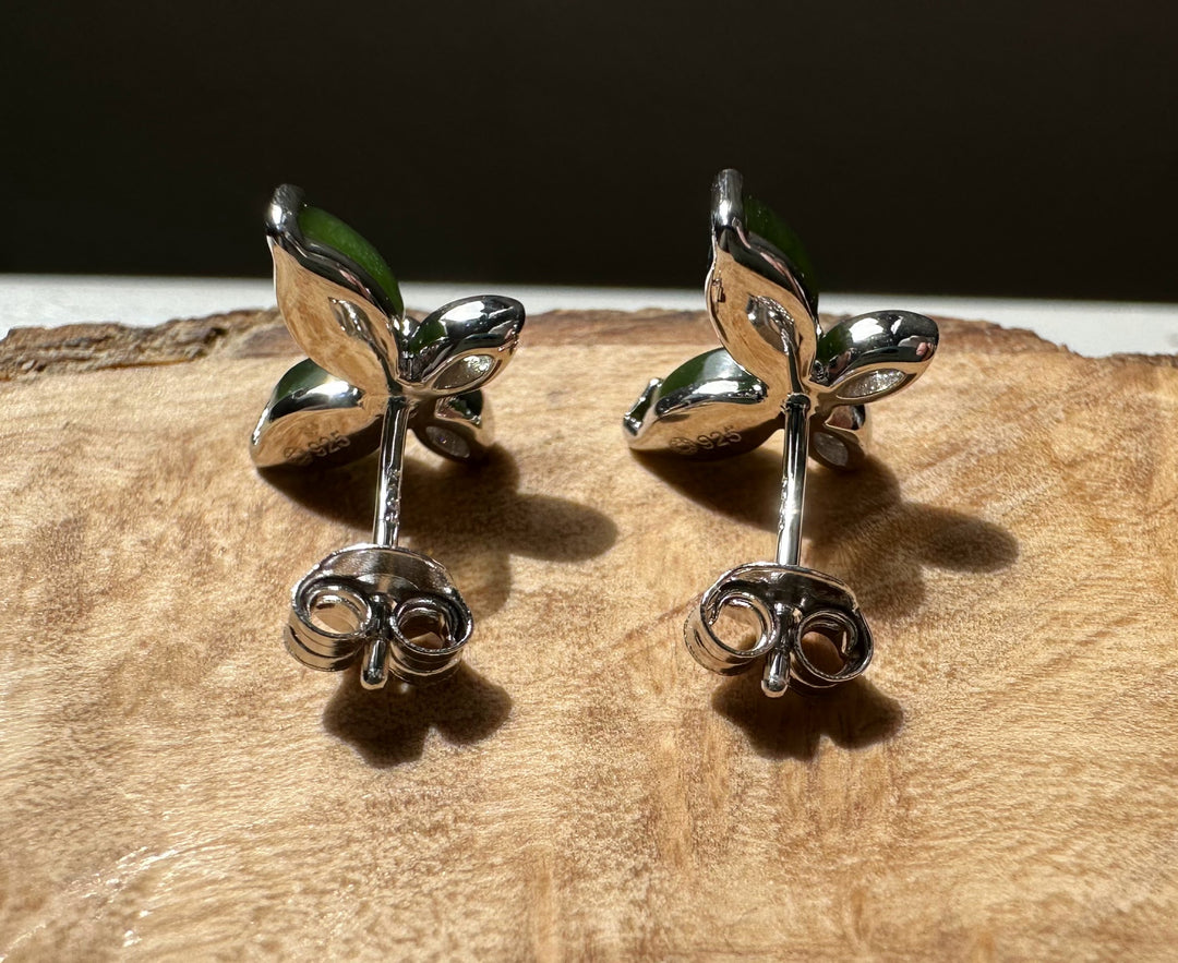 Two silver butterfly stud earrings with green enamel wings and crystal accents on a wooden surface