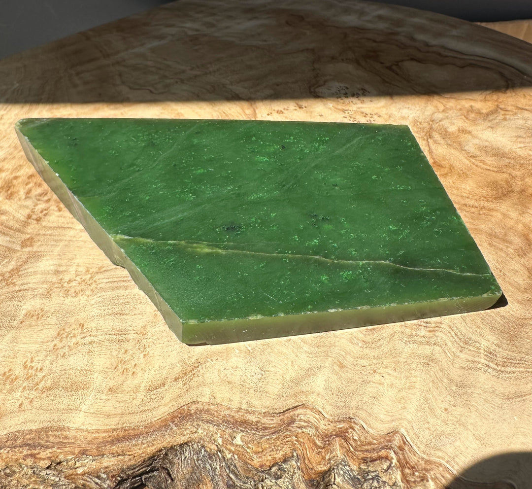 Green jade slab with smooth surface resting on a wooden table, edge visible