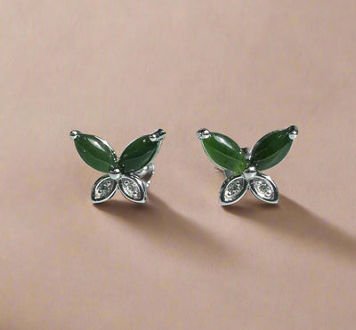 Butterfly-shaped earrings with green wings and silver bodies on a beige background