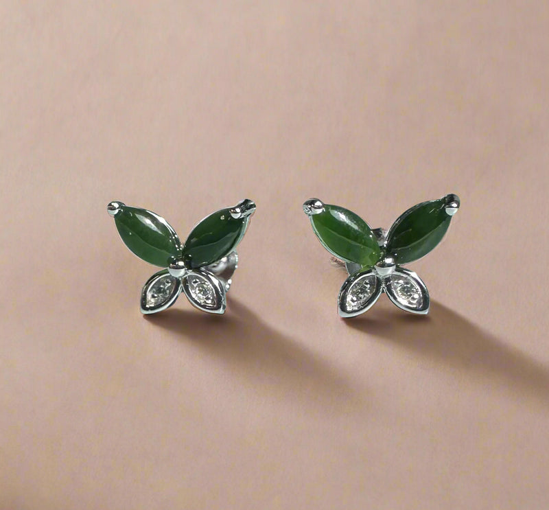 Butterfly-shaped earrings with green wings and silver bodies on a beige background